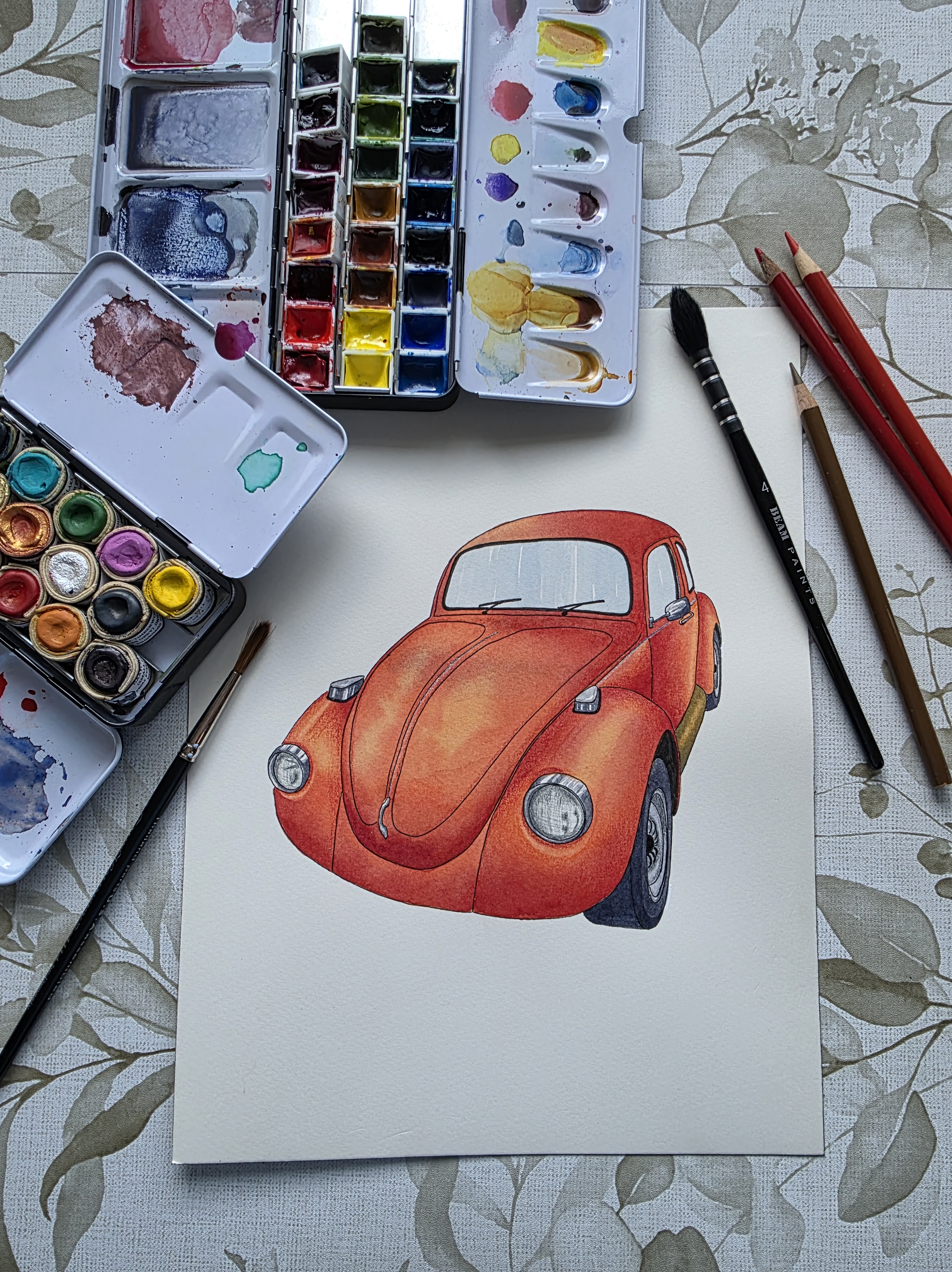 The watercolor painting is placed on a patterned tablecloth next to some water paint and colored pencils. The illustration...